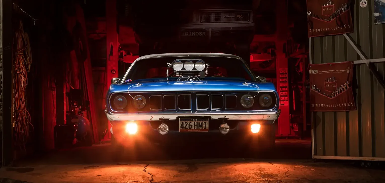 Hot-Rod Performance—blower-equipped blue Plymouth Barracuda in a dim garage, headlights on.