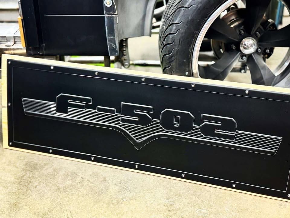 Wicked 53 — custom F-502 bed back-wall panel by Misfit Fabs; machined black plate with linework, rear wheel behind.