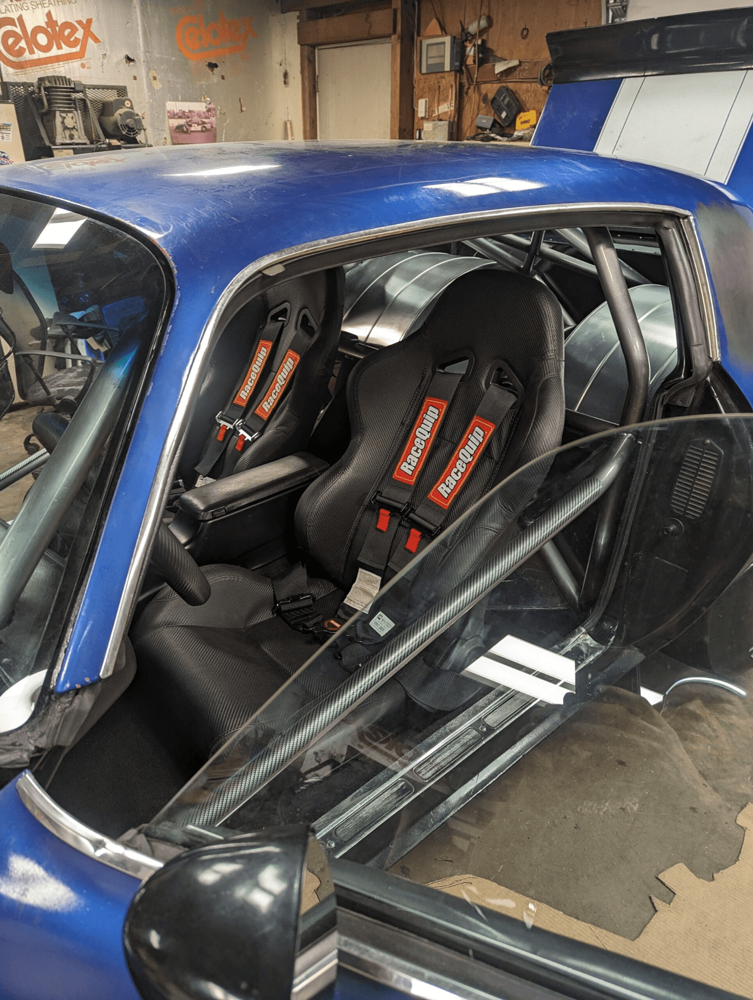 Interior view of a blue Camaro showing RaceQuip racing seats, harnesses, roll cage, and aluminum rear tubs.