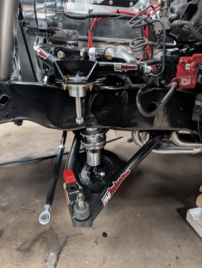 Front suspension close-up showing UMI tubular control arms, coilover setup, and steering components on a performance Camaro build.