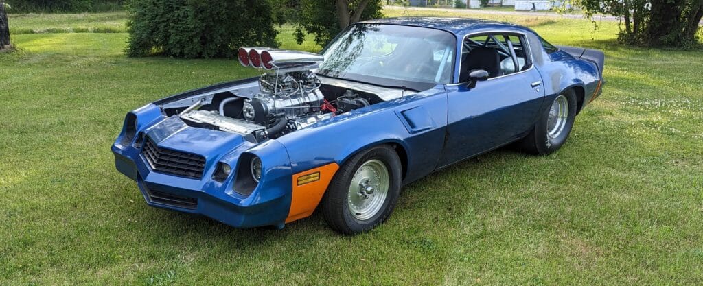 Blown 1980 Camaro Z28 “Pandemic” with an 8-71 supercharged 388 small-block, fat rear tires, and raw steel cage sitting in a yard.
