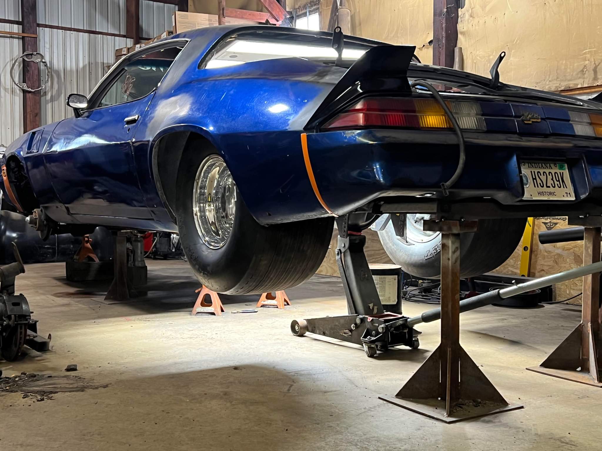 Second-gen Camaro on jack stands in a garage, showing the rear end removed and big slicks tucked under the quarters.