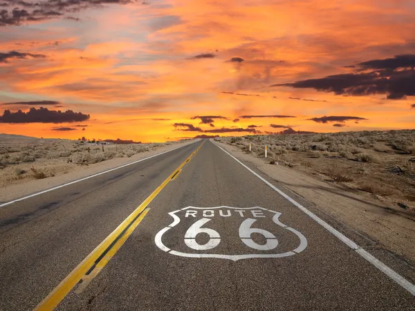 Route 66 highway at sunset with the classic shield logo painted on the road.