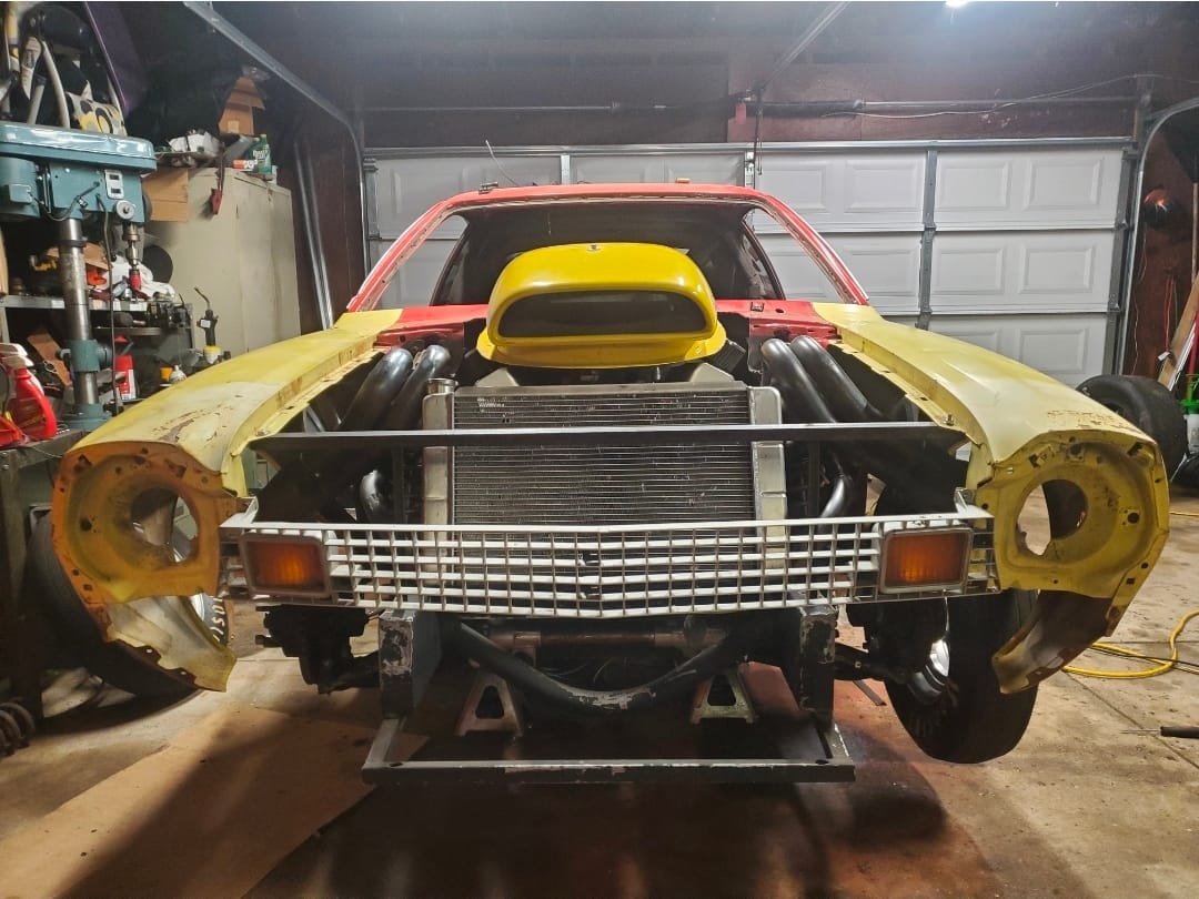 Front view of Team Chinto Ford Pinto in garage with exposed radiator, custom headers, and drag suspension during rebuild