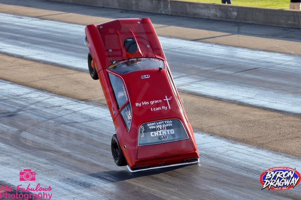 Team Chinto outlaw wheelstanding Pinto riding on the edge, balanced on two wheels mid-pass at Byron Dragway with rear tires visibly off the ground.