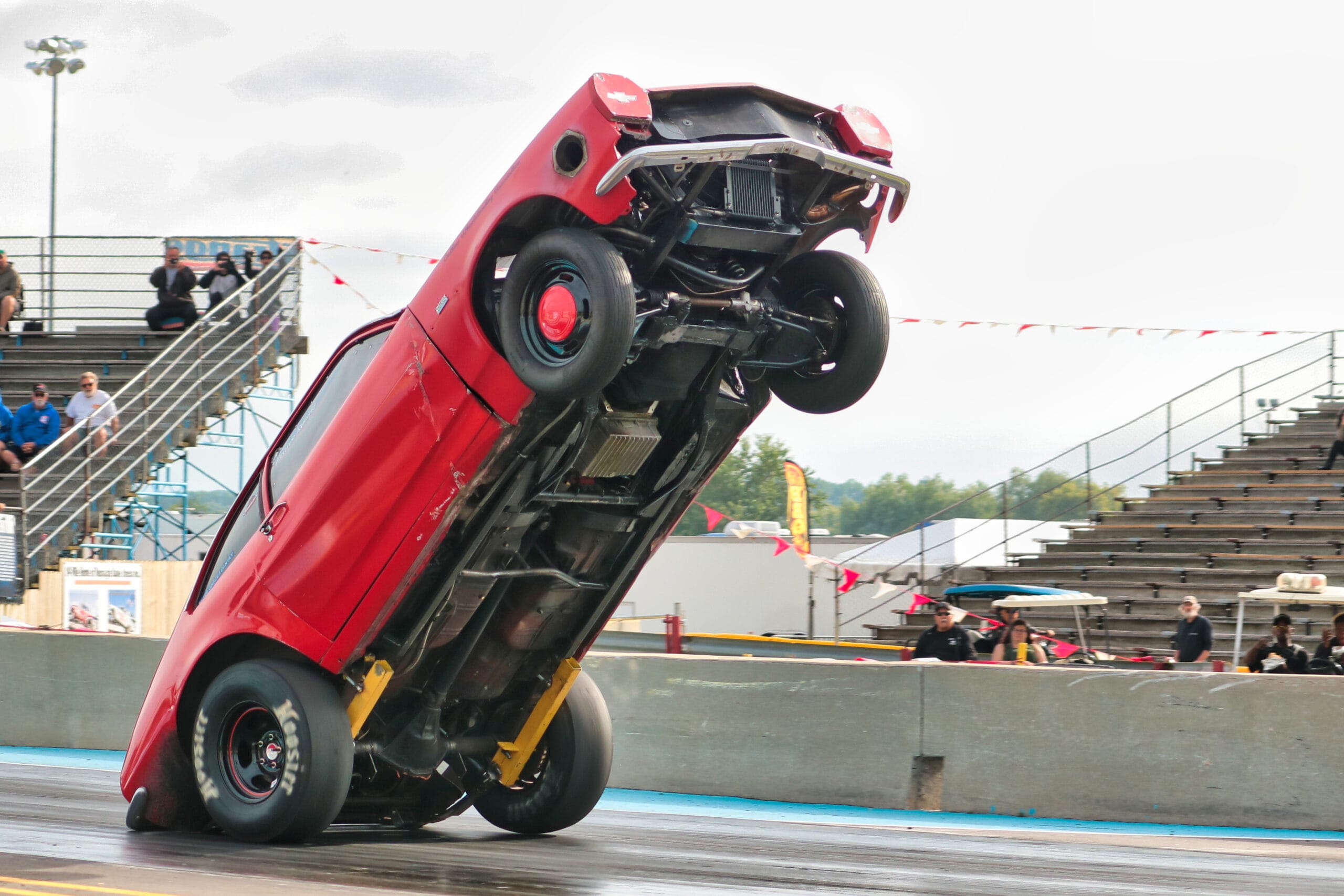 Team Chinto outlaw wheelstanding Pinto nearly rolling over mid-pass, car balanced on the edge with front end violently elevated at the drag strip.